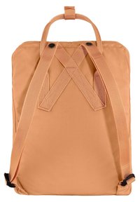 Sac à dos en tissu couleur pêche avec des bretelles en croix, forme rectangulaire, poignée supérieure et bretelles réglables. Extérieur texturé.