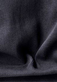 Svart ribbat tyg med vertikala linjer och en mjuk textur, med veck som skapar djup och skugga.