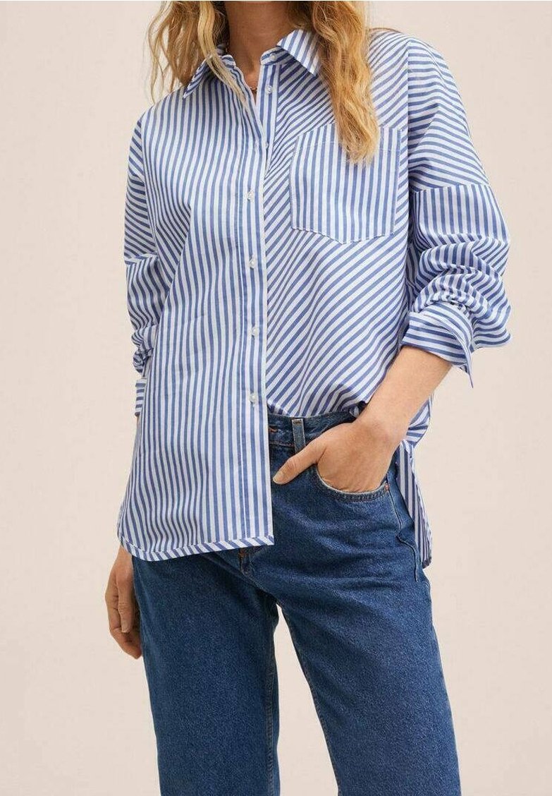Femme portant une chemise à rayures verticales bleu et blanc avec une main dans la poche d'un jean bleu.