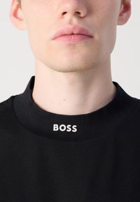 Svart crewneck t-skjorte med ribbestrikket krage og fet hvit "BOSS" logo på halsen. Glatt stoff med en tettsittende design.