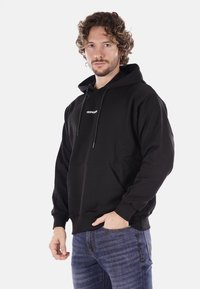 Felpa nera con cappuccio in cotone, dotata di tasca frontale e cordino per il cappuccio, con il logo "PROPAGANDA" in bianco sulla parte anteriore.