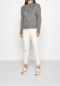 Šedý svetr s pleteným vzorem a kulatým výstřihem, v kombinaci s krémovými tapered kalhotami a světle modrými sandály na podpatku s odhalenými prsty.