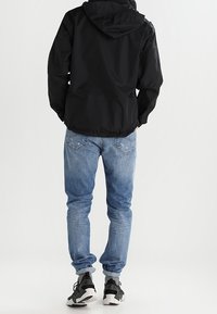 Black hooded jacket, blue denim jeans, and gray-black sneakers. The jacket has a smooth texture; jeans are slightly distressed with a classic fit.