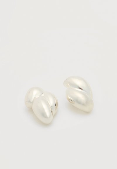 Δύο μικρά, λείους, λαμπερά ασημένια σκουλαρίκια με αφηρημένο σχήμα σε απλό λευκό φόντο.