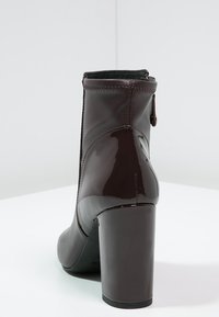 Czarne botki na wysokim obcasie z błyszczącego lakierowanego materiału, gładką teksturą, z tylnym zamkiem i szerokim obcasem.