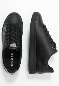 Zwarte sneakers met een gladde, matte afwerking. Kenmerken zijn een logo aan de zijkant, ronde veters en een gestructureerde rubberen zool.