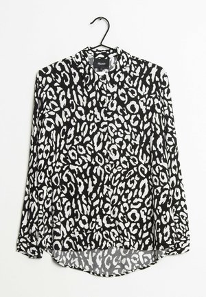 Sort-hvid leopardprint langærmet skjorte med knapper, hængt på en sort bøjle mod en hvid baggrund.