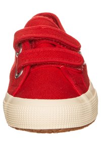 Baskets en toile rouge avec des straps Velcro, bout arrondi, semelle en caoutchouc texturé et bordure en caoutchouc de couleur claire. Design simple avec des accents en métal.