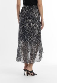 Fustă maxi transparentă, stratificată, cu un model în imprimeu de șarpe, având culori negre, gri și crem. Talie elastică și tiv evazat.
