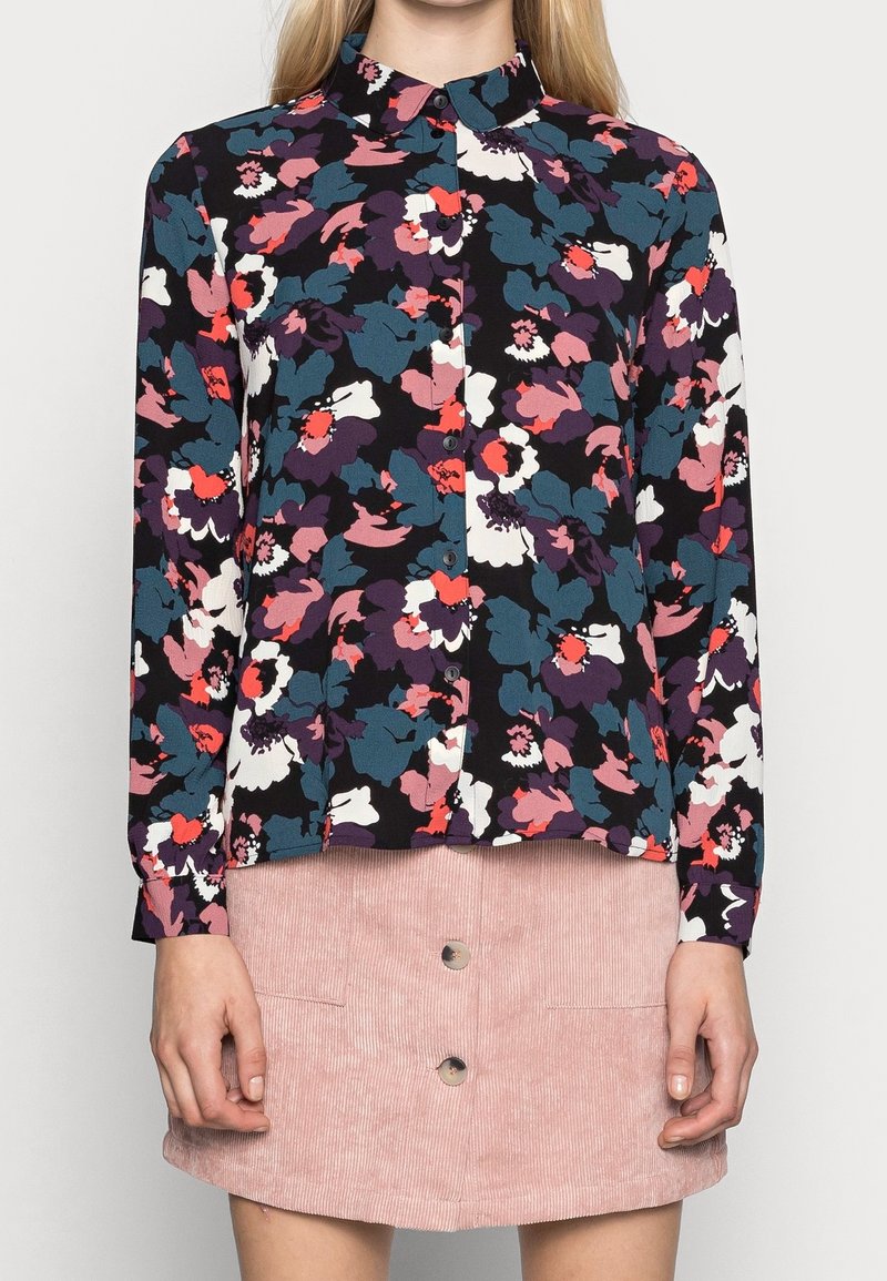 Blusa floreale con bottone su sfondo scuro, caratterizzata da grandi fiori multicolori in rosa, teal e bianco. Maniche lunghe.