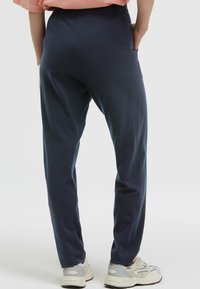 Marineblaue Jogginghosen mit lockerer Passform, elastischem Bund, seitlichen Taschen und einer glatten Textur. Getragen mit hellen Sneakers.