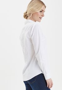 Camicia bianca a maniche lunghe realizzata in tessuto leggero, con colletto button-down, taglio dritto, dotata di yoke posteriore e polsini con bottoni.