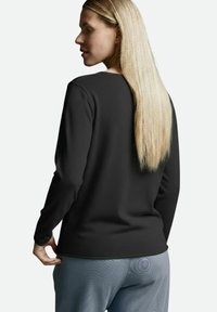 Schwarzes Langarmshirt aus strukturiertem Stoff mit Rundhalsausschnitt und figurbetontem Schnitt, kombiniert mit hellblauen gemusterten Hosen.