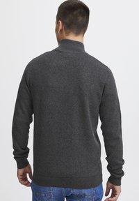 Pullover in maglia grigio scuro con colletto alto, polsini e orlo a coste. Il tessuto appare morbido e con una superficie liscia.