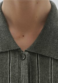 Close-up of a person’s neck wearing a textured gray collared shirt with a button fastened at the top.
