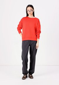Felpa rossa over-size con maniche lunghe, abbinata a pantaloni neri larghi e scarpe con stampa animale. Look semplice e rilassato.