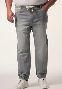 Pantalones jogger gris claro con puños elásticos, cinturilla con cordón, bolsillos laterales y tejido suave y texturizado. Llevados con zapatillas blancas.