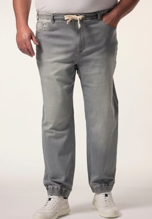 Pantalons de jogging gris clair avec des poignets élastiques, une taille avec cordon de serrage, des poches latérales et un tissu doux et texturé. Portés avec des baskets blanches.