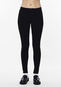 Black stretchy leggings with a high waist, featuring classic five-pocket design and a smooth, matte finish. Paired with black loafers.