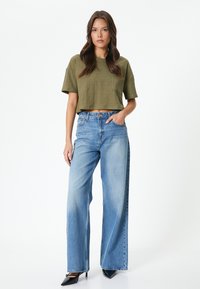 Top texturizado verde oliva cortado, combinado con jeans de tiro alto y pierna ancha de color azul claro y tacones negros de punta.