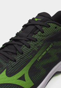 Κοντινή λήψη ενός μαύρου και πράσινου παπουτσιού τρεξίματος με μαύρα κορδόνια, που φέρει την επιγραφή «LIGHTNING SELECT» και πράσινη ριγέ σχεδίαση στο πλάι.