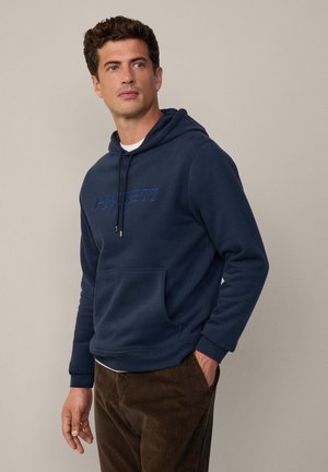 Sudadera con capucha azul marino con un bolsillo frontal, que presenta un logo "HACKETT" en azul contrastante. Fabricada con tejido suave y de corte relajado.