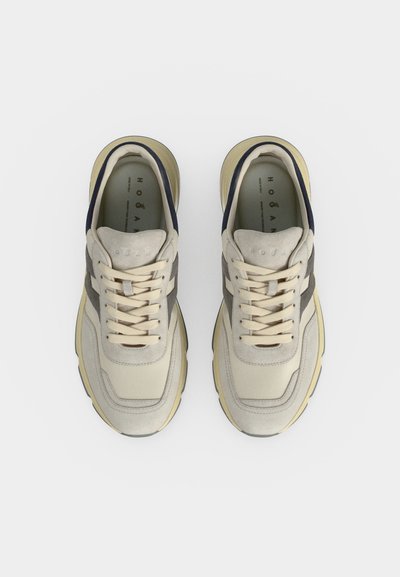 Paire de baskets beiges et grises à lacets vues de dessus sur un fond blanc uni.