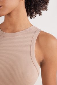 Top sin mangas de color beige con textura acanalada, que presenta un escote redondeado. Primer plano de los detalles del hombro y el escote, con costuras limpias.