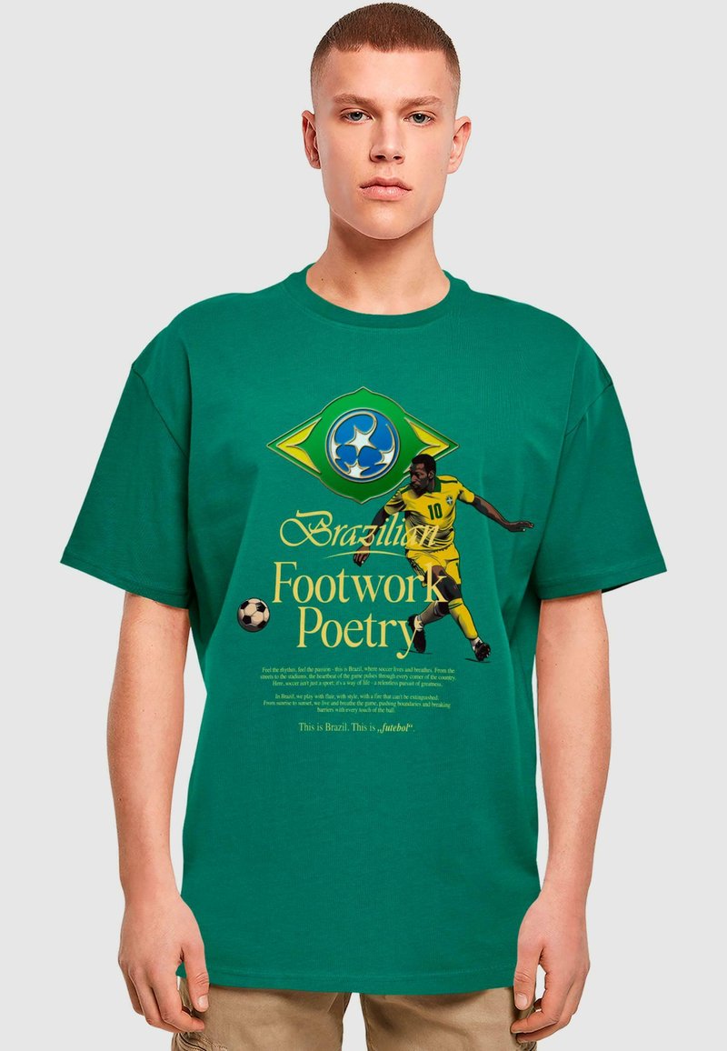 Vihreä puuvillapaita, jossa on jalkapalloilijan graafinen kuva. Tekstissä lukee "Footwork Poetry" ja brasilialaisia symboleja. Lyhythiha, rento malli.