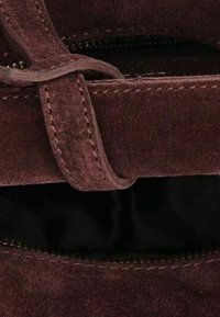 Gros plan sur une sangle en cuir suédé marron avec des détails de couture sur un fond en tissu noir, montrant la texture et la boucle de la fermeture.