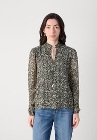 Bluză florală neagră și crem, cu guler înalt, mâneci lungi dintr-un material transparent și detalii cu fundă în față. Asortată cu blugi din denim albastri.