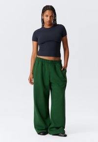 Tamsiai mėlynas glaudus trumpomis rankovėmis viršus ir laisvos tamsiai žalios kelnės su elastinga juosmens juosta, dėvimos su juoda avalyne. Paprastas ir kasdienis dizainas.