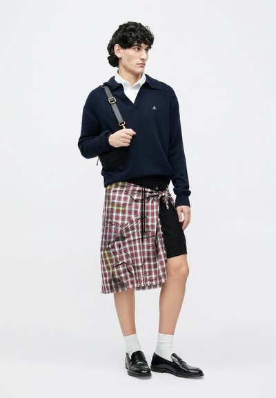 Tumesinine kampsun, valge kraega särk, punase ja rohelise toonides ruuduline ümberpandav seelik, all mustad lühikesed püksid, mustad mokassiinid, kantud valgete sokkidega.