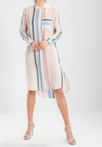 Robe chemise longue avec des rayures verticales multicolores. Fabriquée en tissu léger, elle présente un col et une poche poitrine.