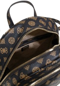 Mochila negra con patrón de logo dorado, cremalleras y forro de tela. El interior cuenta con un bolsillo con cremallera y un diseño con logo impreso sobre tela beige.
