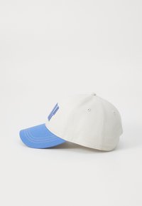 Baseball cap made of fabric, featuring a cream crown and blue visor. Embroidered letters on the front, with visible stitching details.