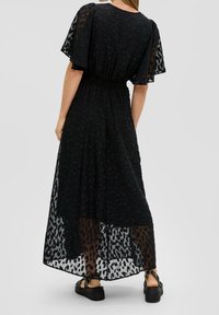 Černé maxi šaty s průhlednou leopardí potištěnou vrstvou, elastickým pasem, krátkými volánkovými rukávy a plochými černými sandály. Hladká textura látky.
