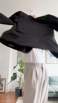Blouson noir au tissu lisse, porté sur une chemise blanche, associé à un pantalon clair, présenté dans une pose dynamique.