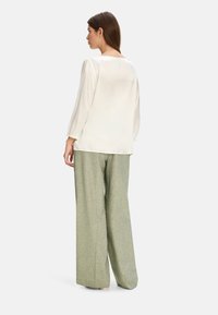 Cream silk blouse with puffed sleeves, paired with loose green textured trousers. Back view highlights soft fabric and relaxed fit.