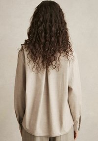 Licht beige lange mouwen shirt met een relaxte pasvorm, gestructureerde stof en knoopmanchetten, met een licht gebogen zoom aan de achterkant.