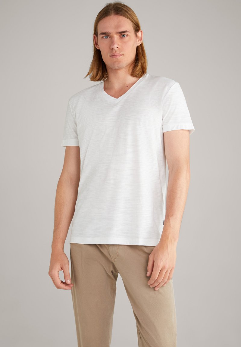 T-shirt blanc à col en v fabriqué à partir d'un tissu texturé, avec des manches courtes et une coupe décontractée. Assorti à un pantalon beige.