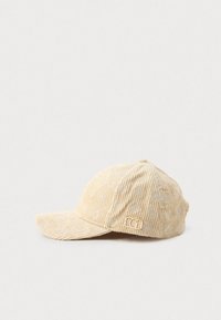 Căciulă de baseball din corduroy bej, cu o suprafață texturată, având un model floral subtil și un accent de logo metalic pe față.