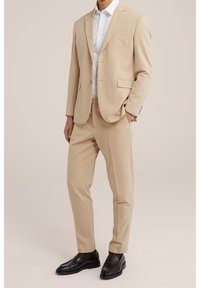 Beige suit with a tailored blazer and matching trousers, paired with a white shirt. Black loafers complete the look.