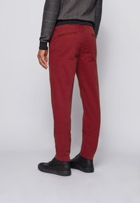 Czerwone bawełniane spodnie o luźnym kroju, z tylnymi kieszeniami i gładką teksturą, zestawione z czarnymi trampkami.