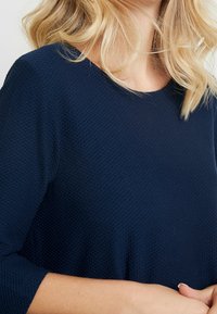 Granatowy, teksturowany top z okrągłym dekoltem i rękawami do połowy przedramienia. Tkanina ma wypukły wzór dla dodatkowego efektu.