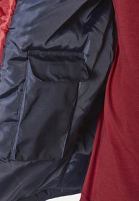 Marineblaues Pufferjackeninnere mit glatter Textur und einer quadratischen Tasche; daneben befindet sich ein roter Stoff, der kontrastierende Farben und Materialien zeigt.