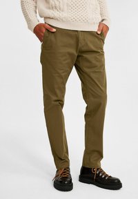 Olijfgroene chino's met een recht onderbeenontwerp, voorzien van zijzakken en een soepele katoenstructuur, gecombineerd met zwarte wandelschoenen en oranje veters.