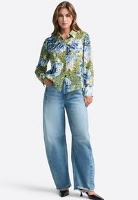 Long-sleeve shirt with a floral pattern in blue and green, paired with light blue wide-leg jeans, and pointed black footwear.