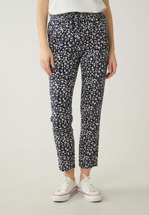 Pantalon marine avec un motif floral blanc, design fuselé, taille élastique et poches latérales, associé à des baskets blanches.