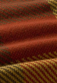 Gros plan sur un tissu en laine doux avec un motif texturé dans des teintes de rouge, orange, jaune et vert, montrant des points de tricot détaillés et des plis.